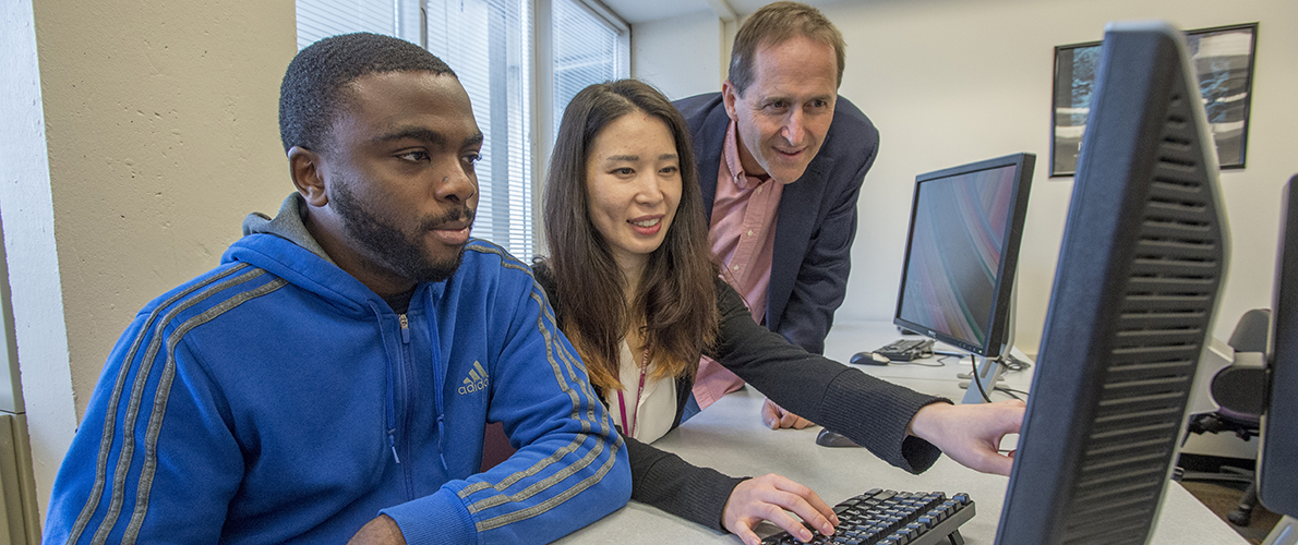 An instructor helping two students with classwork on the computer